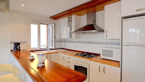 A kitchen with white cabinets, a wooden countertop, a stove, a microwave, and a refrigerator.