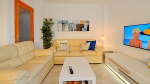 A living room with a beige sofa, a white coffee table, a TV on the wall, and a plant.