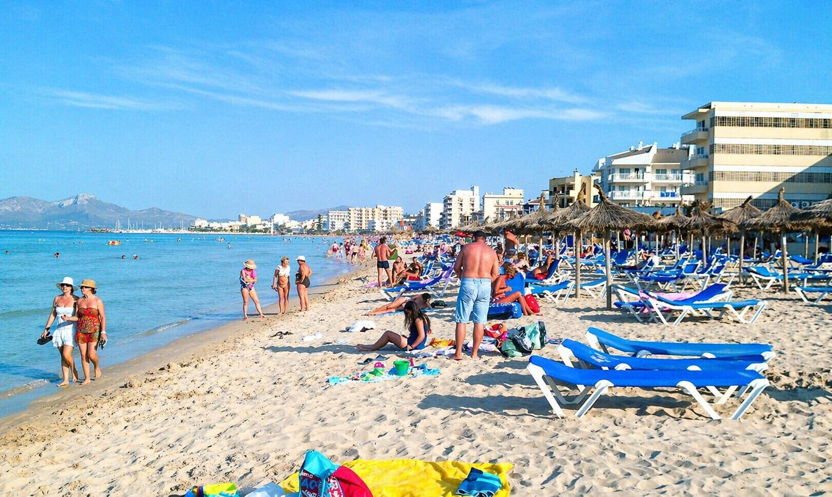 A beach with sun loungers, umbrellas, and people.