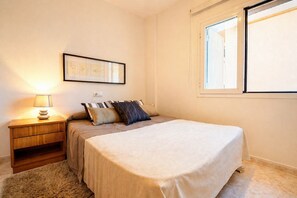 Une chambre à coucher avec un lit, une table de chevet, une lampe, un tableau encadré et une fenêtre.