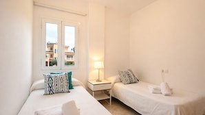 A hotel room with two beds, a nightstand, a lamp, and a window with a view of buildings.