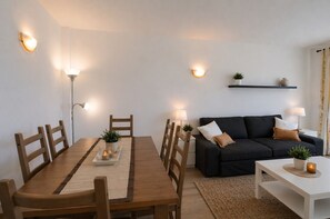 A modern living room with a dining table, sofa, and coffee table, all with minimalistic decor and ambient lighting. - Apartamento en Sa Marina cerca de la playa (Alcúdia)