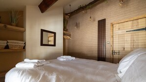 Un lit bien fait, avec du linge de lit blanc, une tête de lit en bois et un miroir au mur.