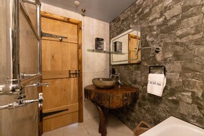 A bathroom with a wooden door, a stone wall, a wooden sink, and a white bathtub.