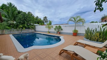 A swimming pool with a white deck, surrounded by potted plants and a white fence.
