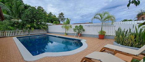 A swimming pool with a white deck, surrounded by potted plants and a white fence.