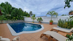Une piscine dotée d’une terrasse blanche, entourée de plantes en pot et d’une clôture blanche.