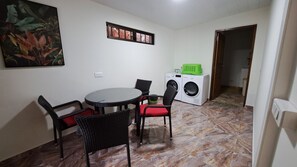 Un petit coin repas avec une table ronde et quatre chaises, un lave-linge et une porte donnant sur une autre pièce.
