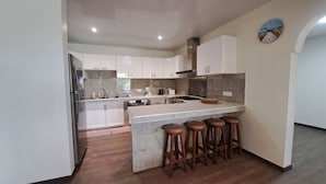Une cuisine moderne avec des meubles blancs, un îlot central doté de tabourets, une cuisinière et un évier.
