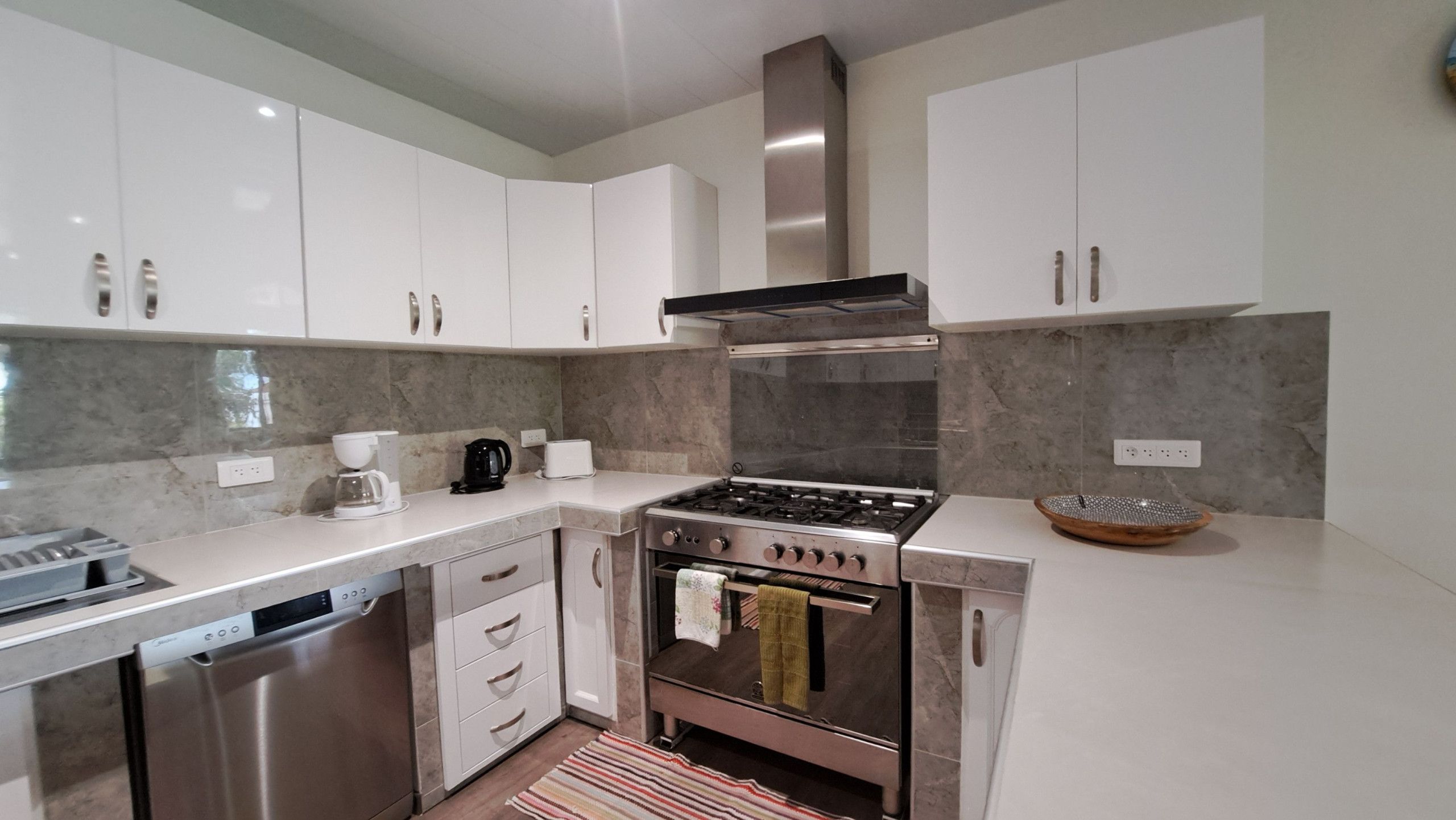 A modern kitchen with stainless steel appliances, white cabinetry, and a marble backsplash.