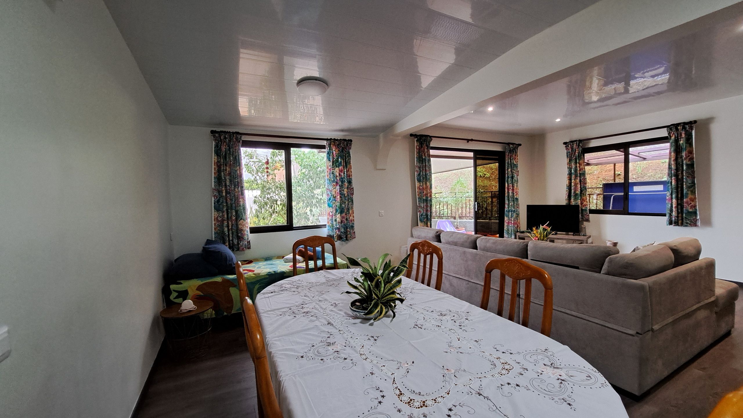 Una sala de estar con una mesa de comedor, sofás, un televisor y una lámpara de techo.