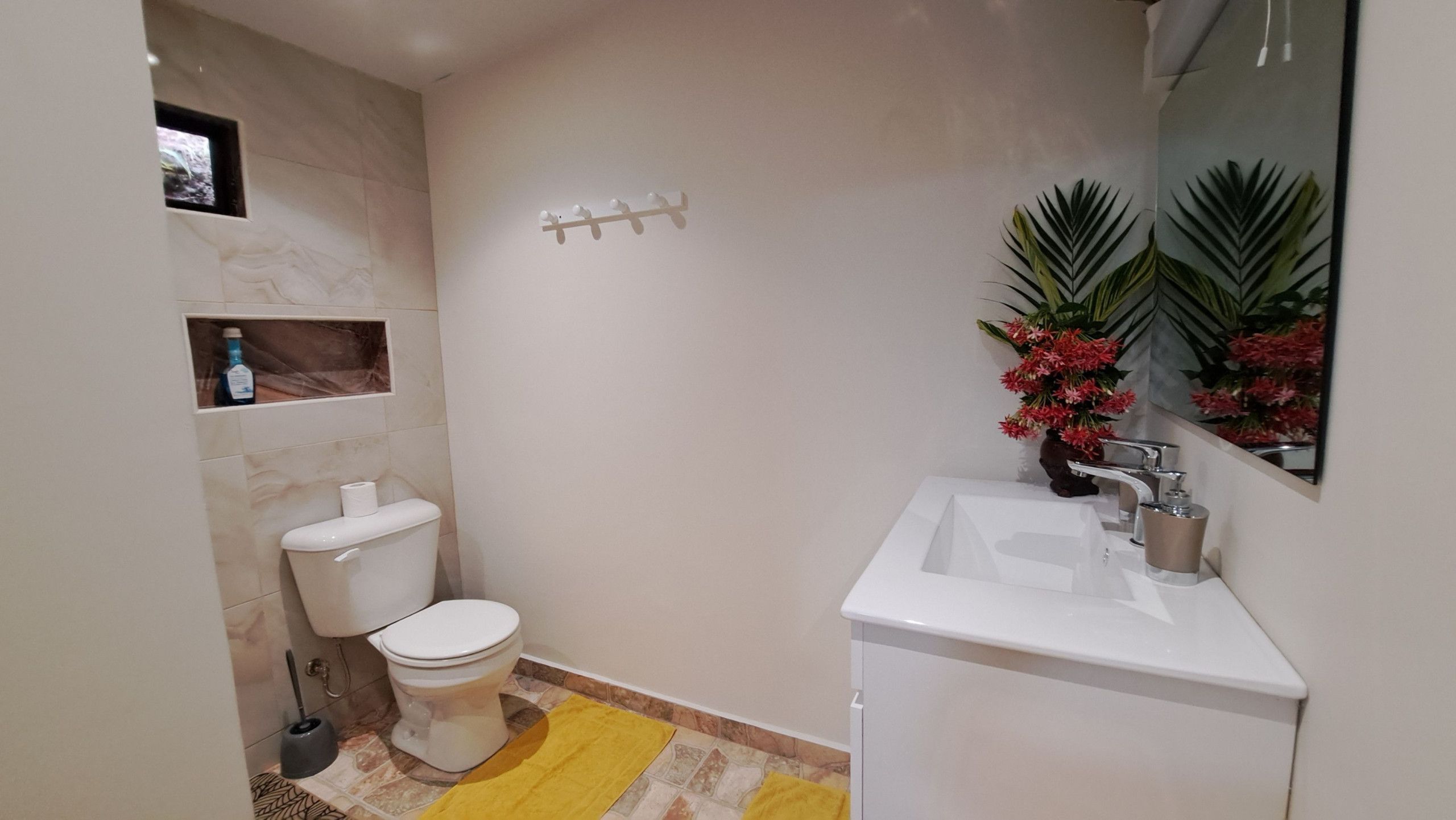 A bathroom with a toilet, sink, and mirror. There is a small shelf with a bottle and a picture frame.