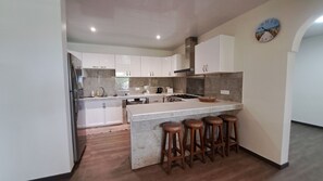 A modern kitchen with white cabinets, a central island with stools, a stove, and a clock on the wall.