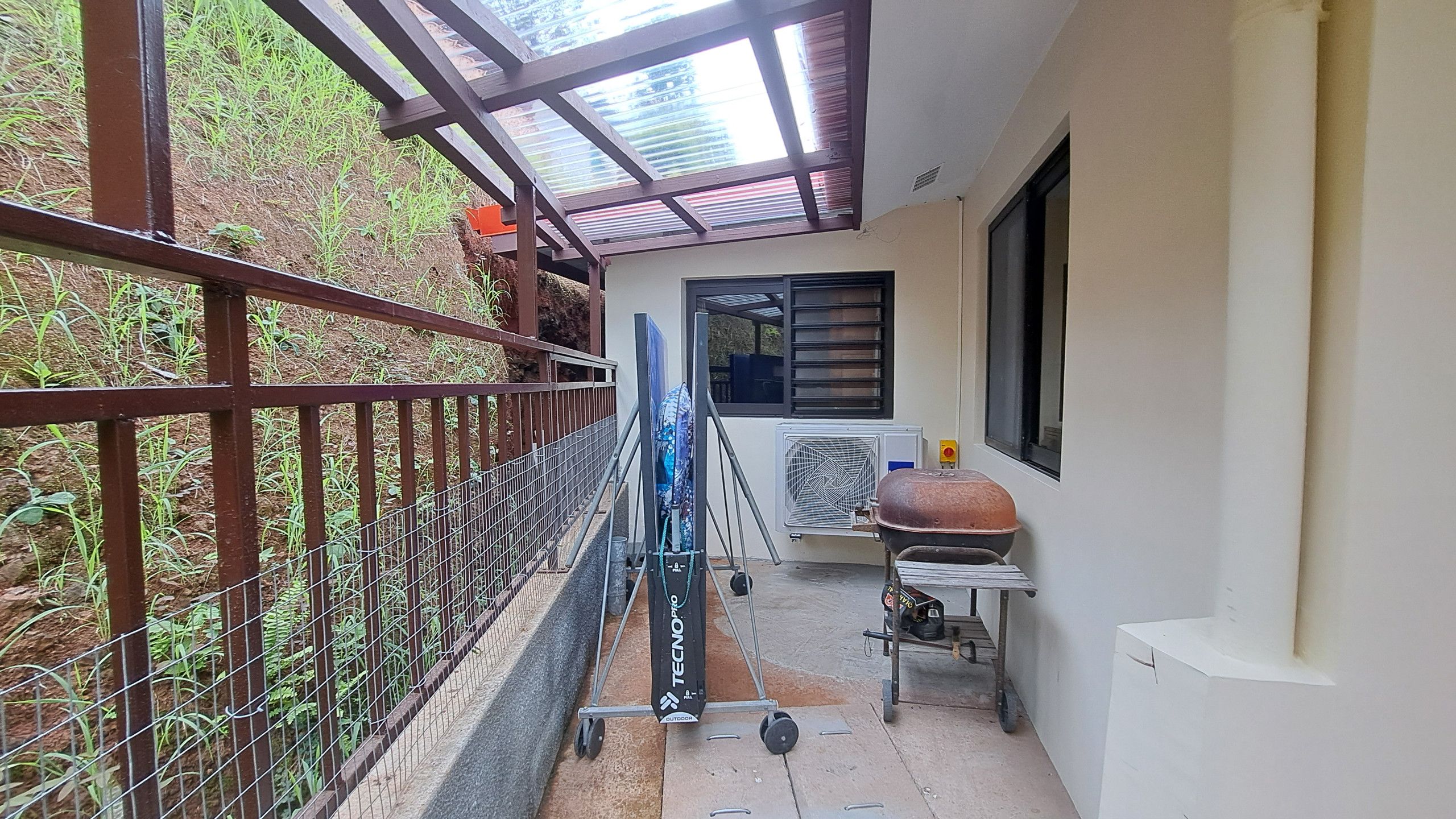 A covered outdoor area with a metal fence, a grill, and a cart with a blue umbrella.