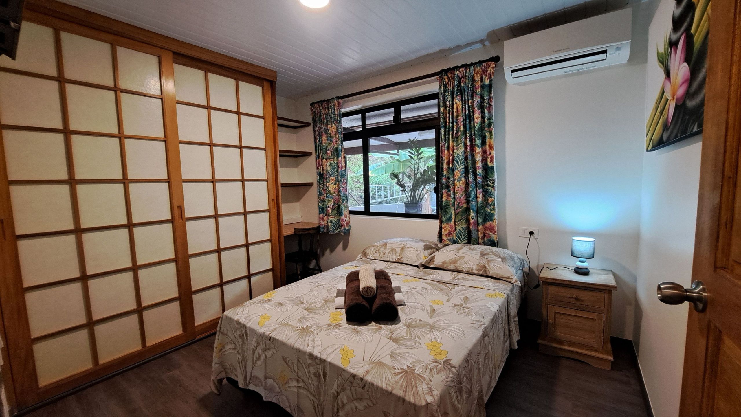 A bedroom with a bed, a nightstand, a lamp, a window with curtains, and a sliding door.