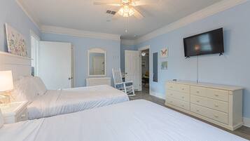 Un dormitorio con dos camas, ventilador de techo, cómoda y televisor en la pared.