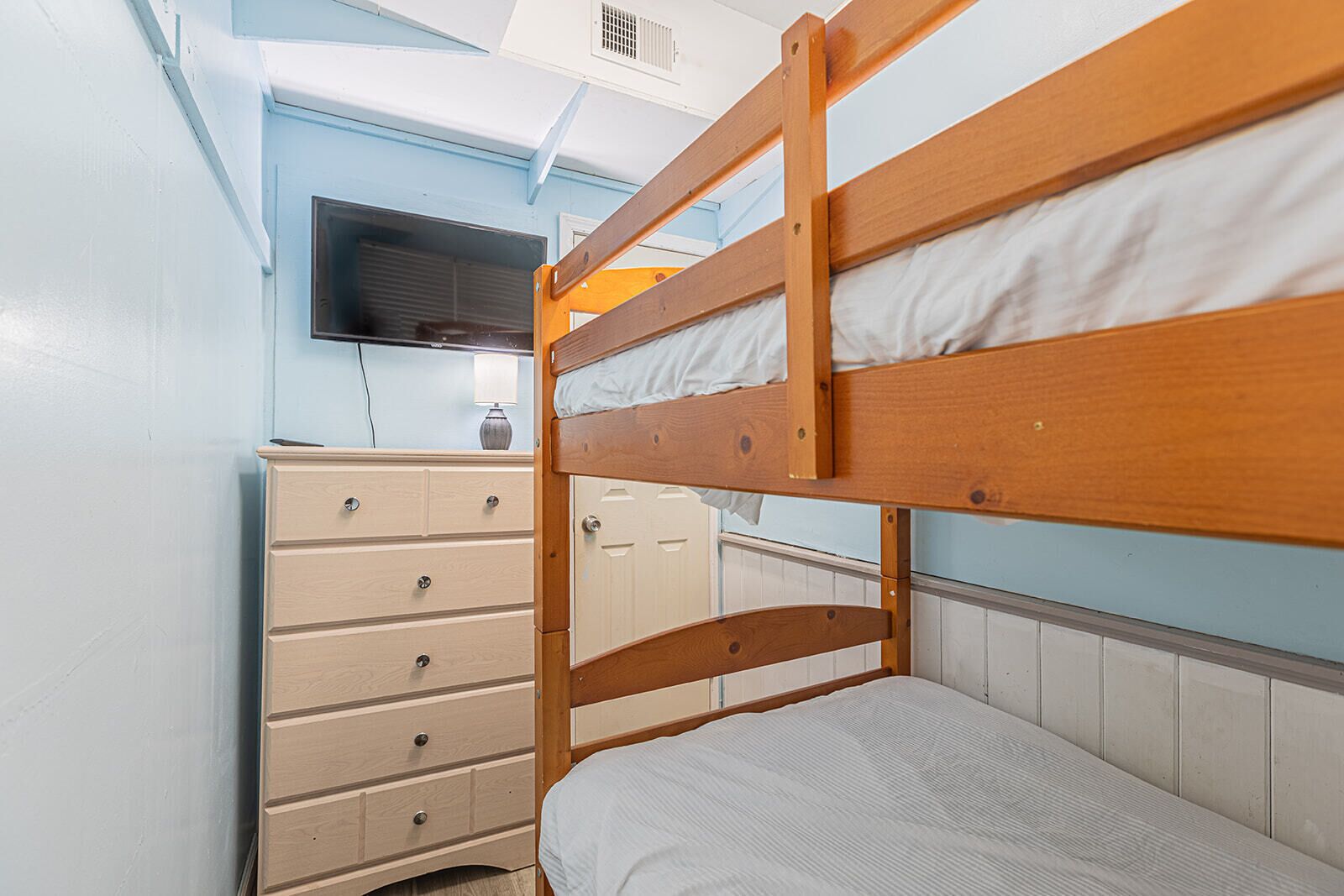 A bunk bed with a wooden frame, a dresser with multiple drawers, and a television mounted on the wall.