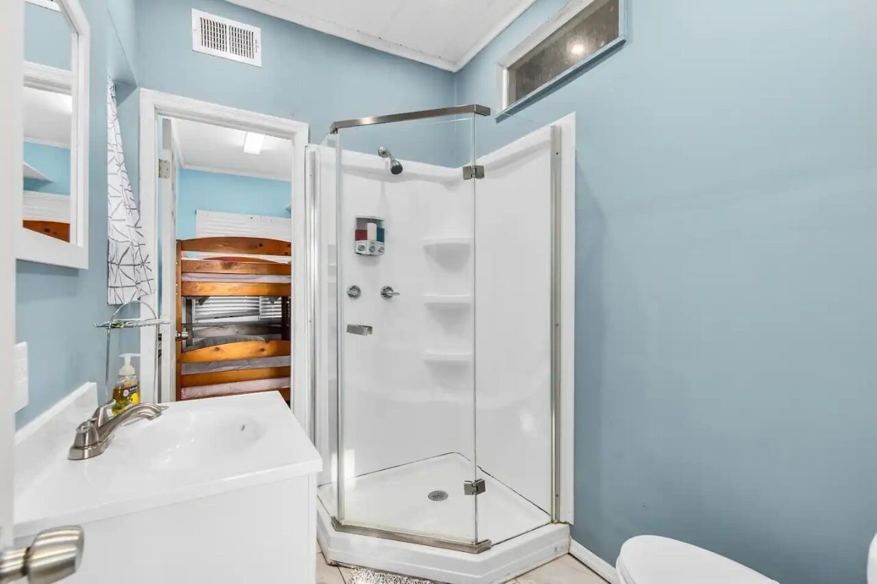 Een badkamer met een douche in een glazen cabine, een witte wastafel en een houten opbergmeubel.