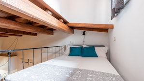 A bedroom with a bed, a patterned bedspread, and wooden beams above.
