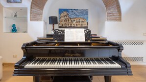 A grand piano in a room with a mural of the Colosseum, a glass shelf with decorative items, and a music stand with sheet music.