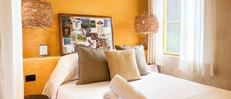 A neatly made bed with pillows, a wall art collage, and a window with curtains.