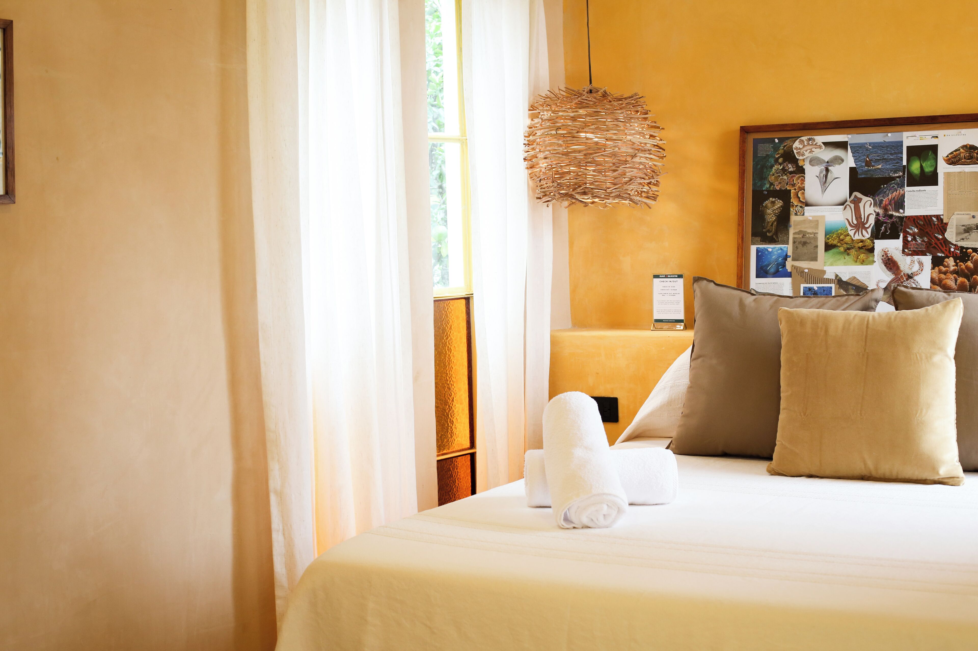 A hotel room with a bed, pillows, a bulletin board, and a window with curtains.