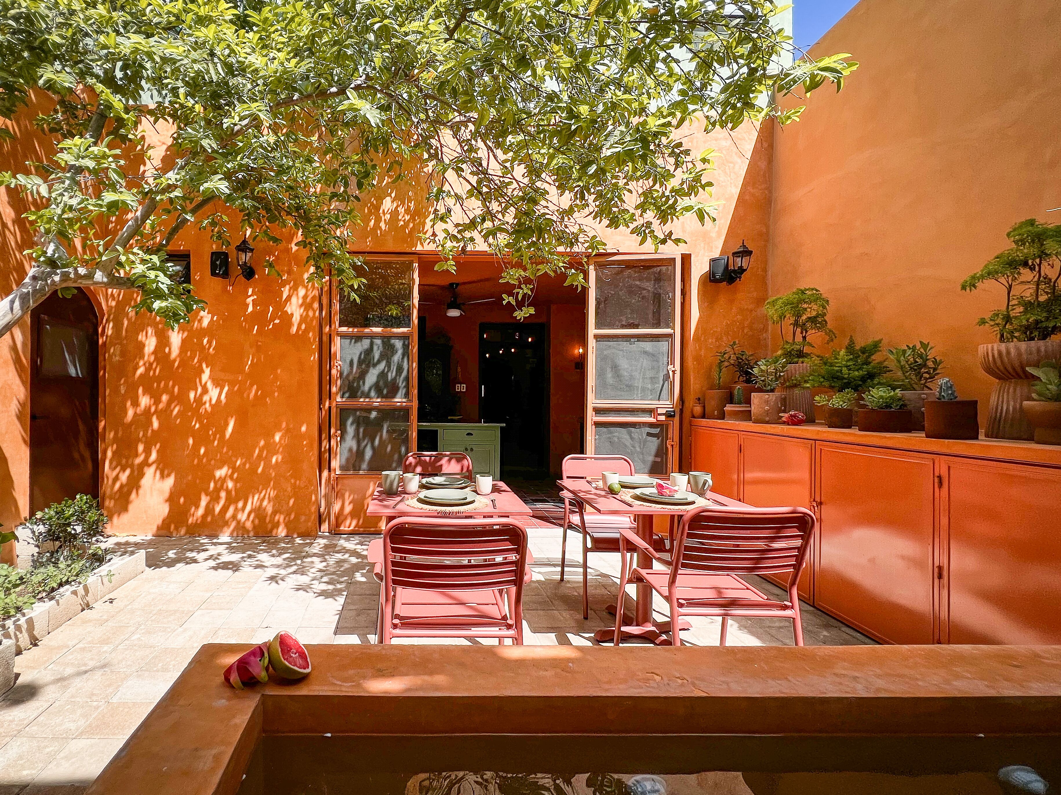 Un patio al aire libre con mesa y sillas, rodeado de paredes anaranjadas y plantas en macetas.