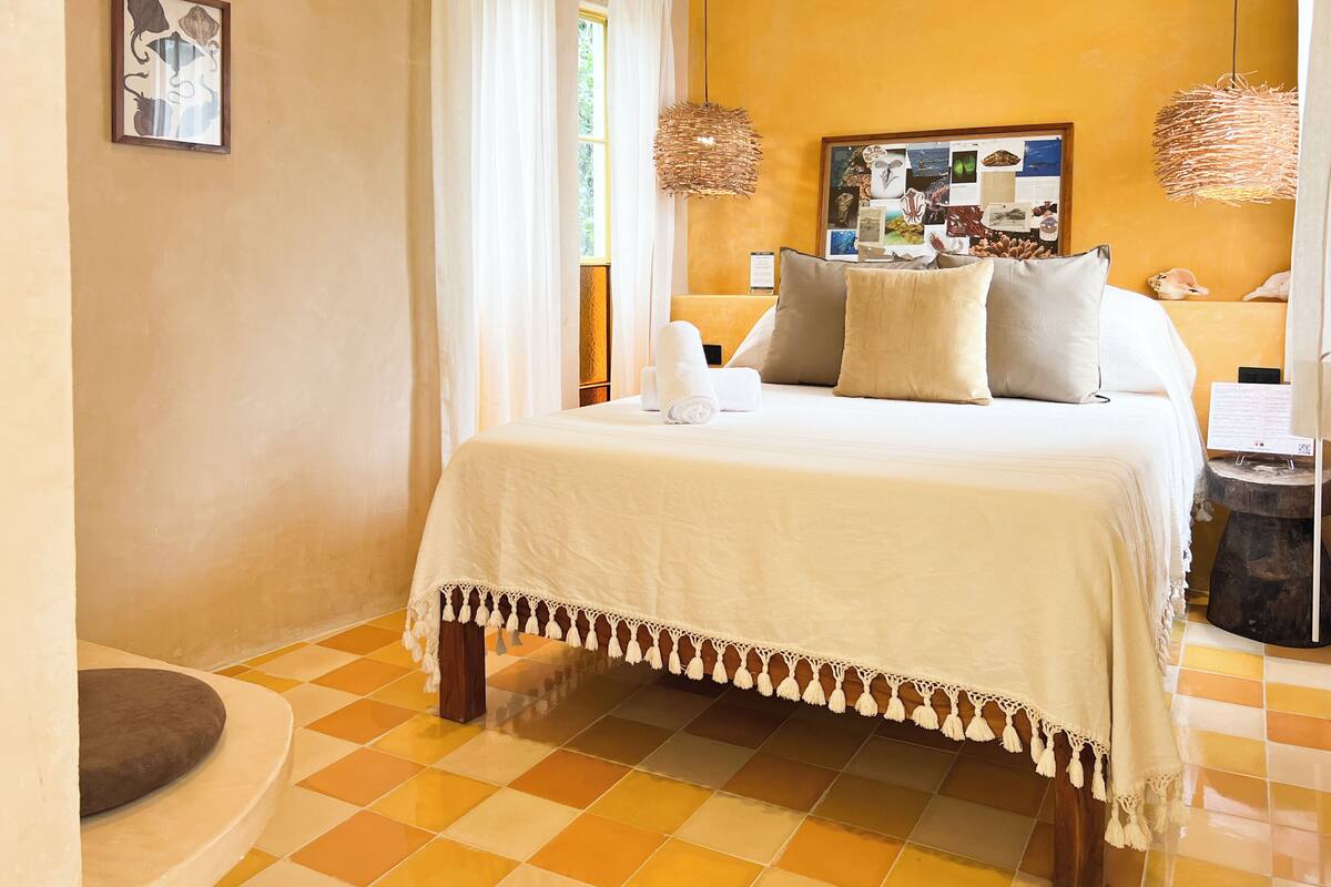 A neatly arranged bedroom with a bed, pillows, a bedside table, and a wall-mounted artwork.
