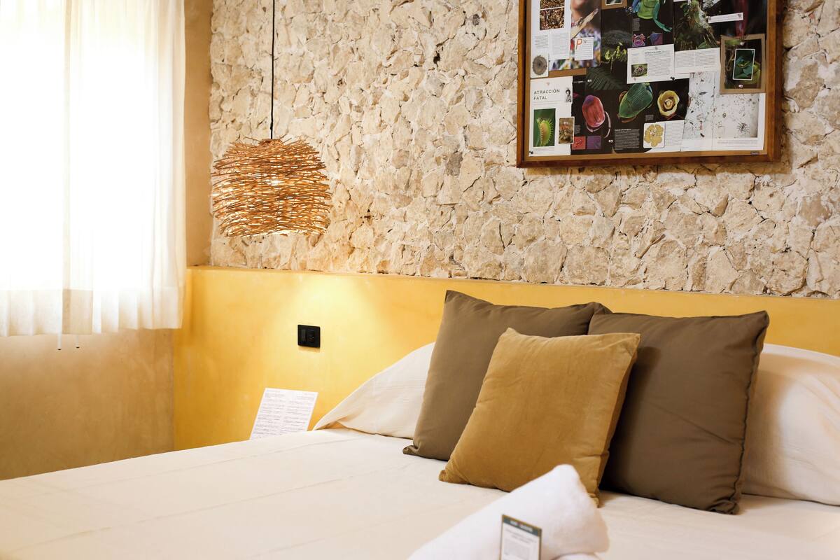 A neatly made bed with two pillows, a wall-mounted information board, and a woven light fixture.