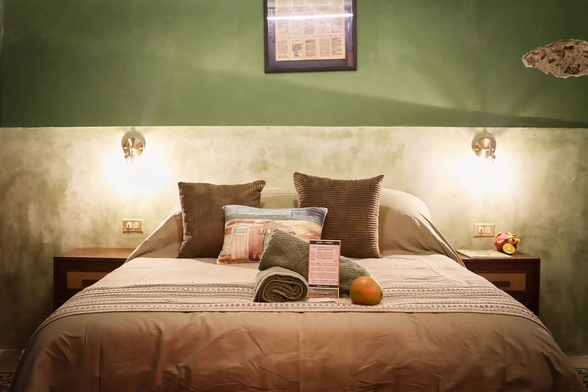 A neatly made bed with a beige comforter, two pillows, a folded towel, a fruit, and a framed menu on the nightstand.