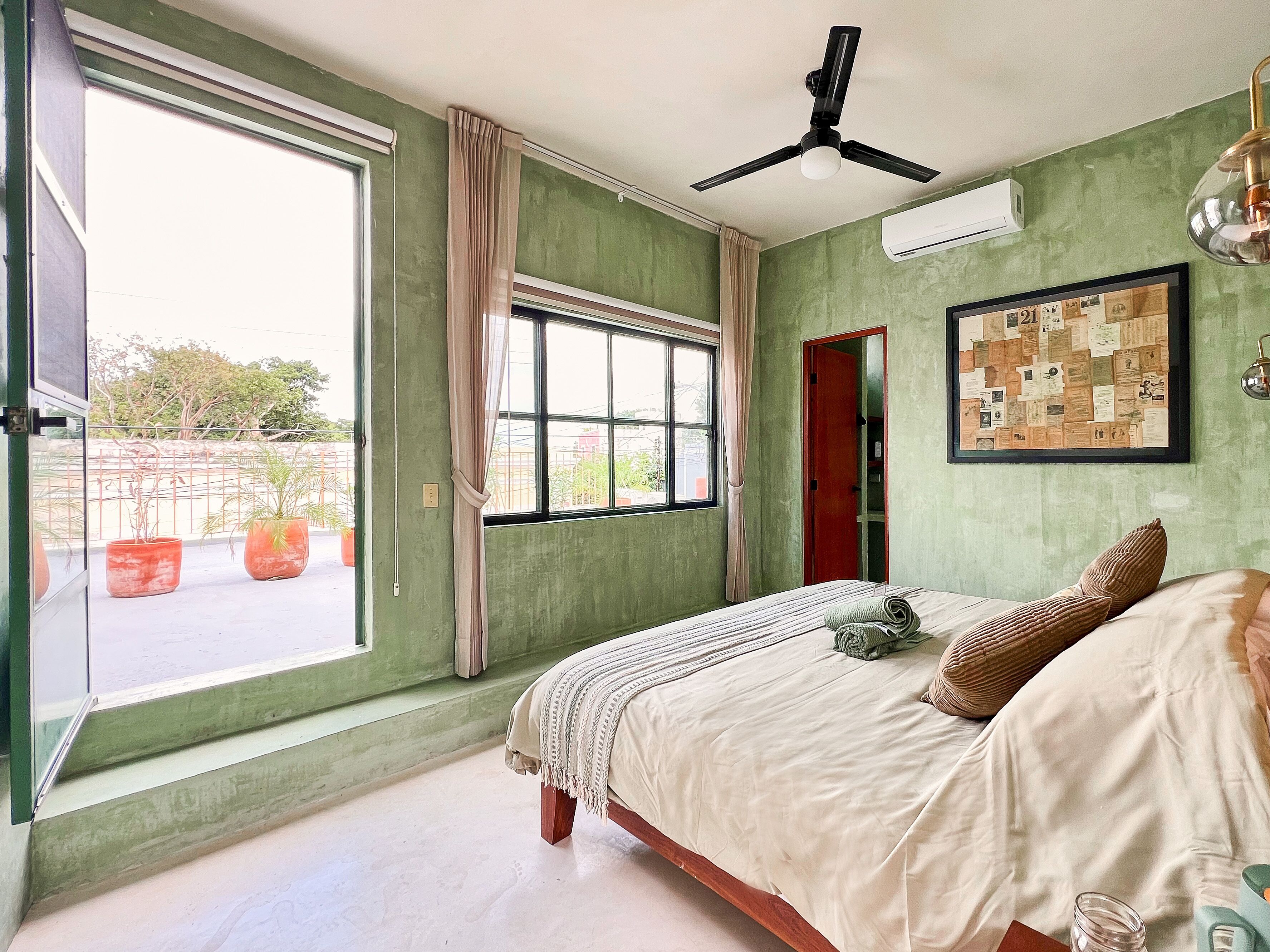 A bedroom with a bed, a ceiling fan, a window with curtains, and a wall-mounted air conditioner.