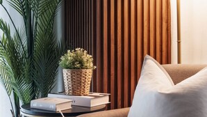 Ein modernes Wohnzimmer mit grauem Sofa, einer weißen Lampe, einer Wand aus Holzleisten und einem Topfpflanzen.