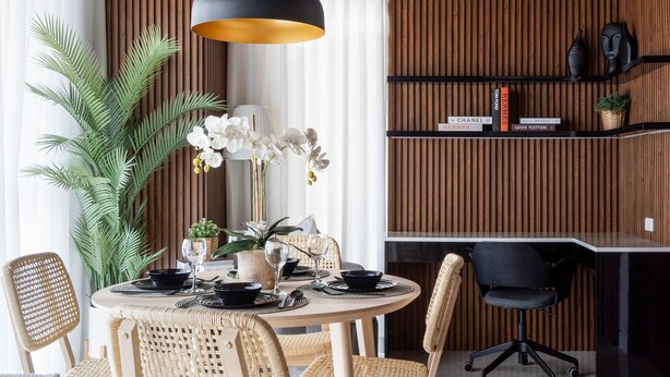 Ein Essbereich mit einem runden Tisch, Stühlen, einer schwarzen Pendelleuchte, einem Blumentopf und einem Bücherregal mit Büchern und Dekoration.