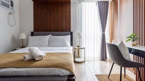 Ein modernes Hotelzimmer mit einem großen Bett, Nachttischlampen, einer Wandpaneele aus Holz, einer Essecke mit einem Stuhl und einer Topfpflanze.