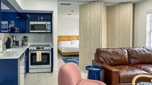 Ein modernes Hotelzimmer mit Küchenzeile, einem braunen Ledersofa, einem Bett mit Holz-Kopfteil und einer blauen Akzentwand.