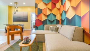 Una sala moderna con un sofá modular, una mesa de centro de madera y un diseño geométrico colorido en la pared.