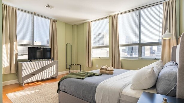 Un dormitorio con cama, televisor, cómoda y ventana con cortinas.
