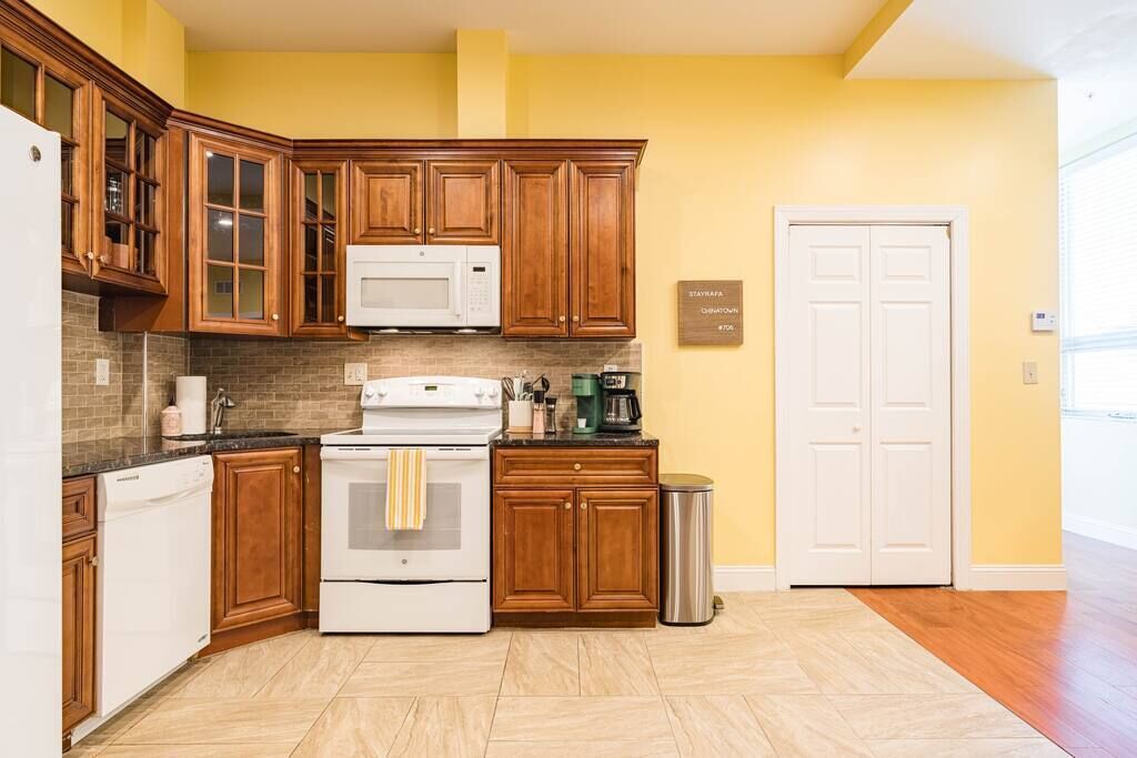 Une cuisine avec des meubles de rangement en bois, un four à micro-ondes, une cuisinière et une poubelle.