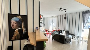 Moderni olohuone, jossa on ruokailutila. Tilaa hallitsee suuri taulu, ja siellä on myös sohva, sohvapöytä sekä seinälle asennettu televisio.