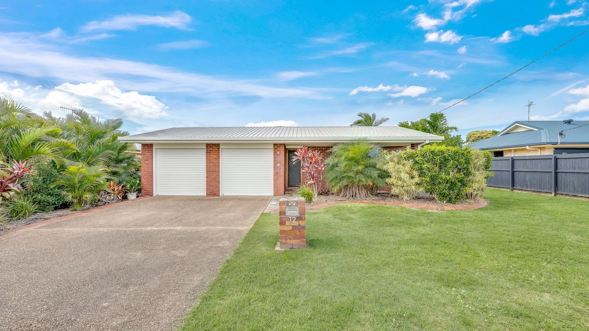 A residential house with a garage, a well-maintained lawn, and various tropical plants.