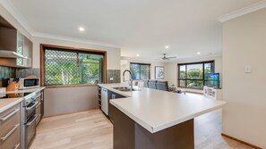 Une cuisine moderne dotée d’un îlot central, d’appareils électroménagers intégrés et de grandes fenêtres offrant une vue sur la verdure.