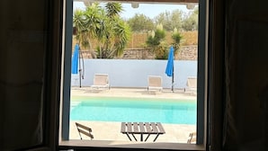 Blick auf ein Schwimmbecken mit Liegestühlen und Sonnenschirmen, eine Steinmauer und eine Holzbalkendecke.