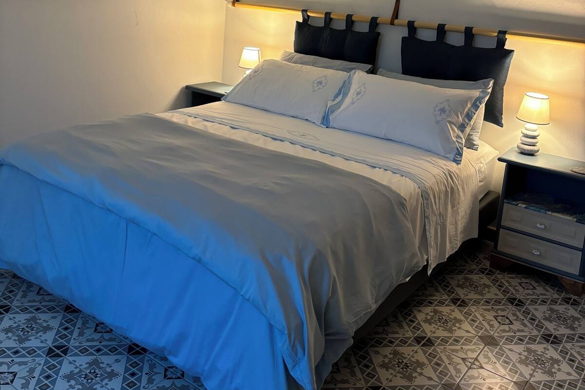 Un letto rifatto con una coperta blu, due lampade sui comodini e un comodino con una lampada.