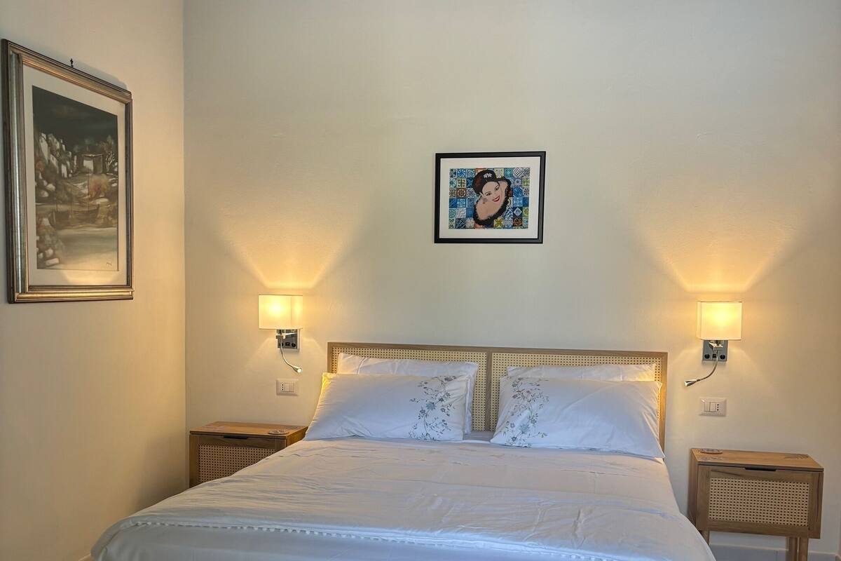 Una camera da letto con un letto di legno, due comodini, una lampada a parete e un quadro incorniciato.