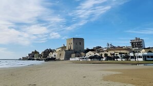 Eine Küstenstadt mit einem markanten historischen Turm, einem Sandstrand und einer Mischung aus Wohnhäusern.