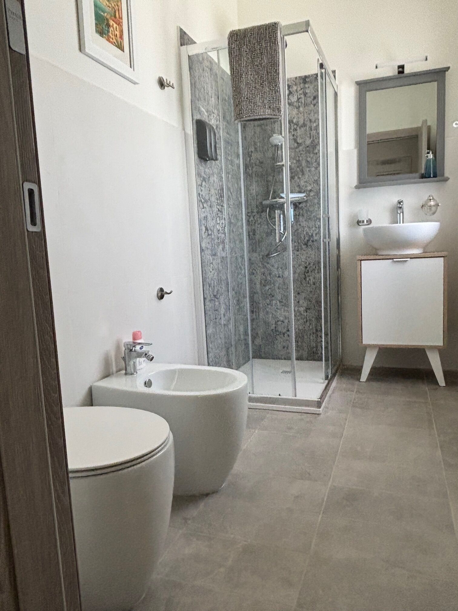 Een badkamer met een douche met glazen wand, twee witte wastafels en een toilet.