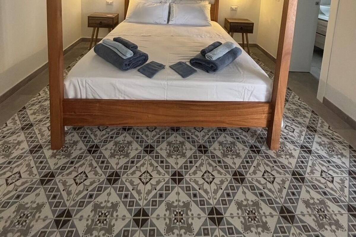 Un letto a baldacchino con pavimento a motivi geometrici, due comodini e un quadro appeso al muro.