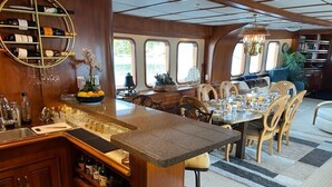A spacious dining area with a long table and chairs, a bar area with a wine rack, and a view through large windows.