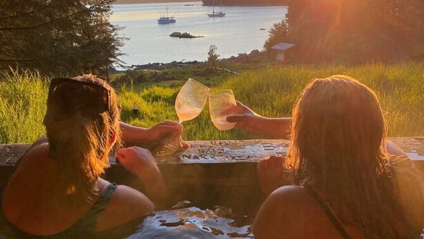 Two people sitting by a pool with a sunset view of boats on the water.