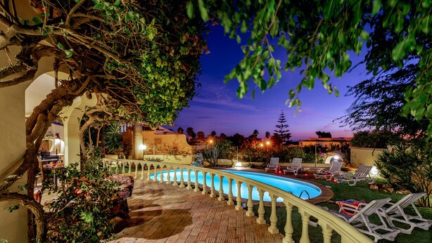 A swimming pool with a curved design, surrounded by a wooden deck and a white balustrade. - Peaceful villa with pool & BBQ (Albufeira)